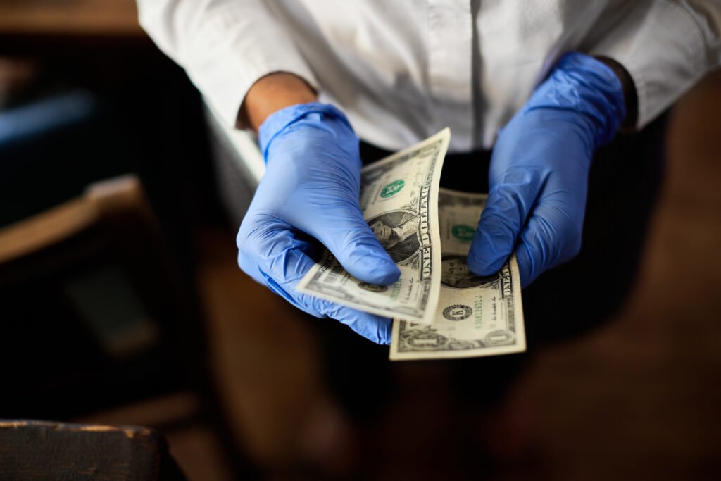 Close-up of waitress wearing protective gloves while counting money in a cafe.
